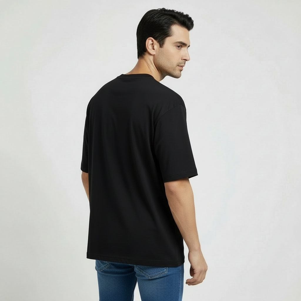 Man wearing a black oversized t-shirt and blue jeans on a light gray background