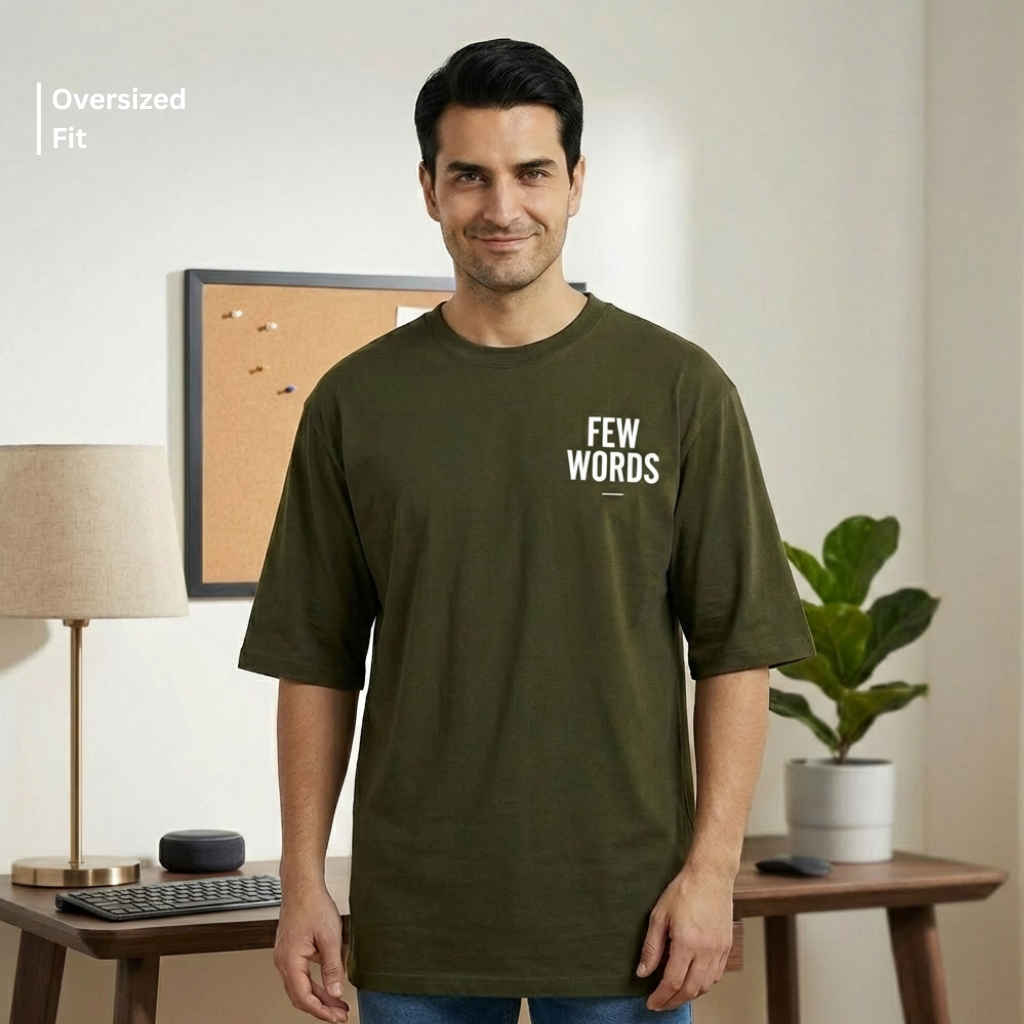 Man wearing an olive green t-shirt with 'FEW WORDS' text in a home office setting