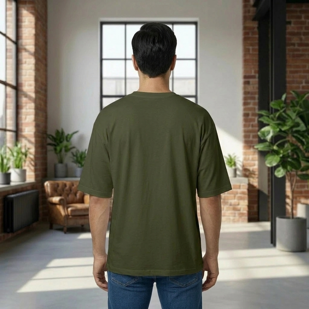 Person wearing an olive green t-shirt in a modern indoor setting with plants and a couch.