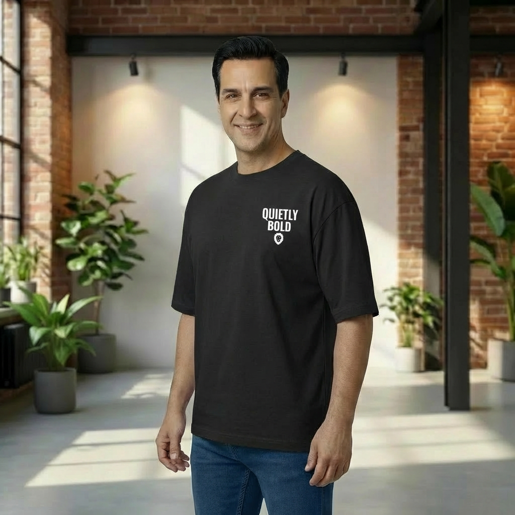 Man wearing an oversized black t-shirt with 'Quietly Bold' text in a modern indoor setting with plants.