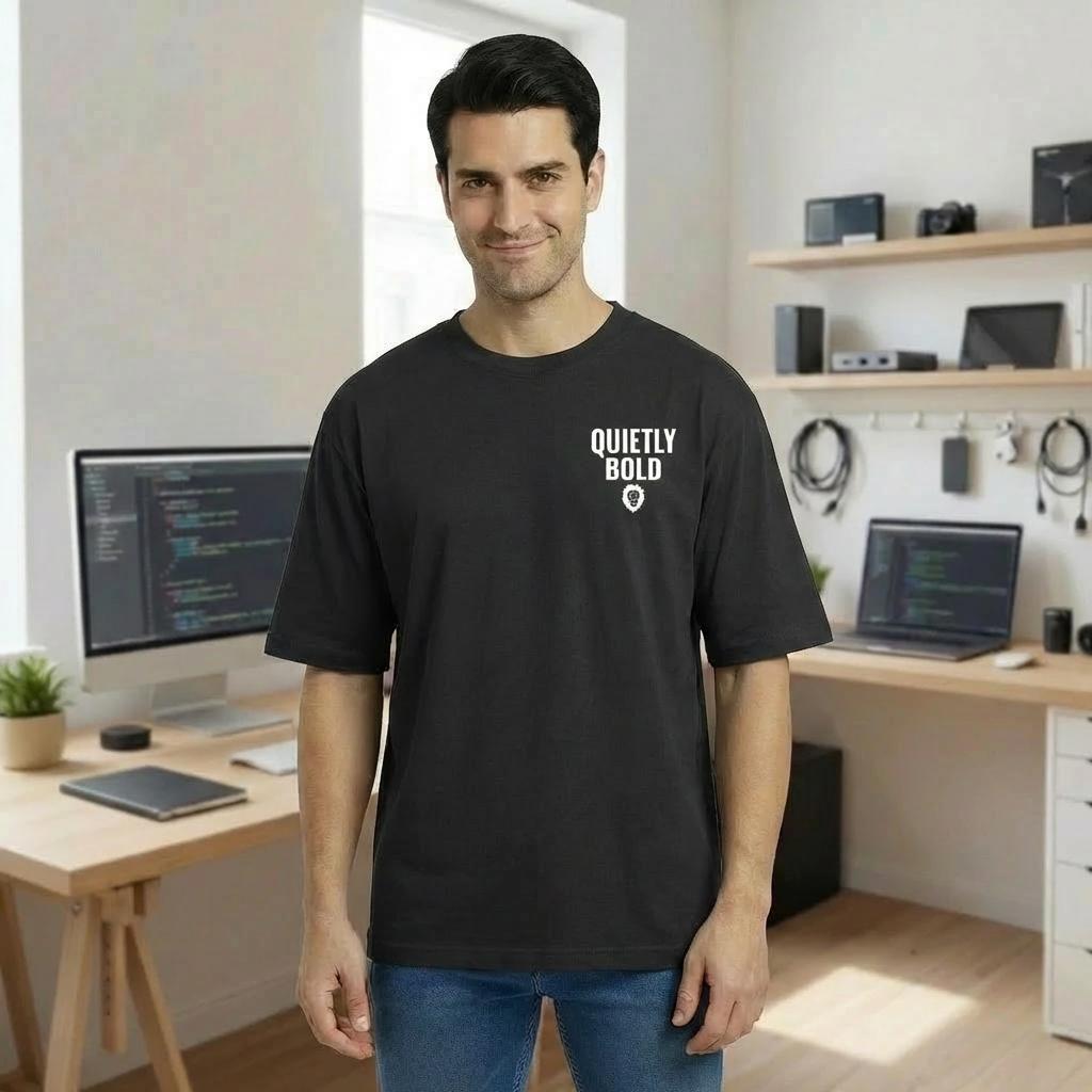 Man wearing an oversized black t-shirt with 'Quietly Bold' text in a home office setting