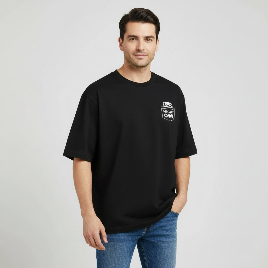 Man wearing a black  oversized t-shirt with a lnight owl ogo on a light gray background